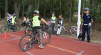 Umundurowany policjant pośród dzieci z rowerami i na rowerach.