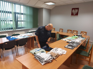 Policjant przegląda zabezpieczoną odzież w pokoju Komendy Powiatowej Policji w Wieruszowie.