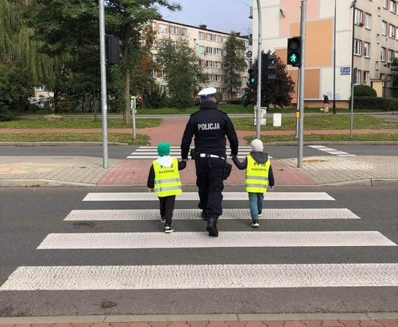 policjantka prowadzi dzieci po przejściu dla pieszych.