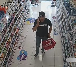 mężczyzna trzymający telefon komórkowy w jednej ręce a w drugiej koszyk na zakupy,ubrany w szare spodnie i czarną koszulkę.