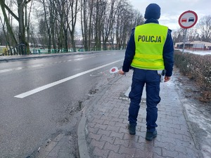 policjant podczas nadzoru nad ruchem drogowym, stoi na chodniku a w ręku trzyma tarczę do zatrzymywania pojazdów.